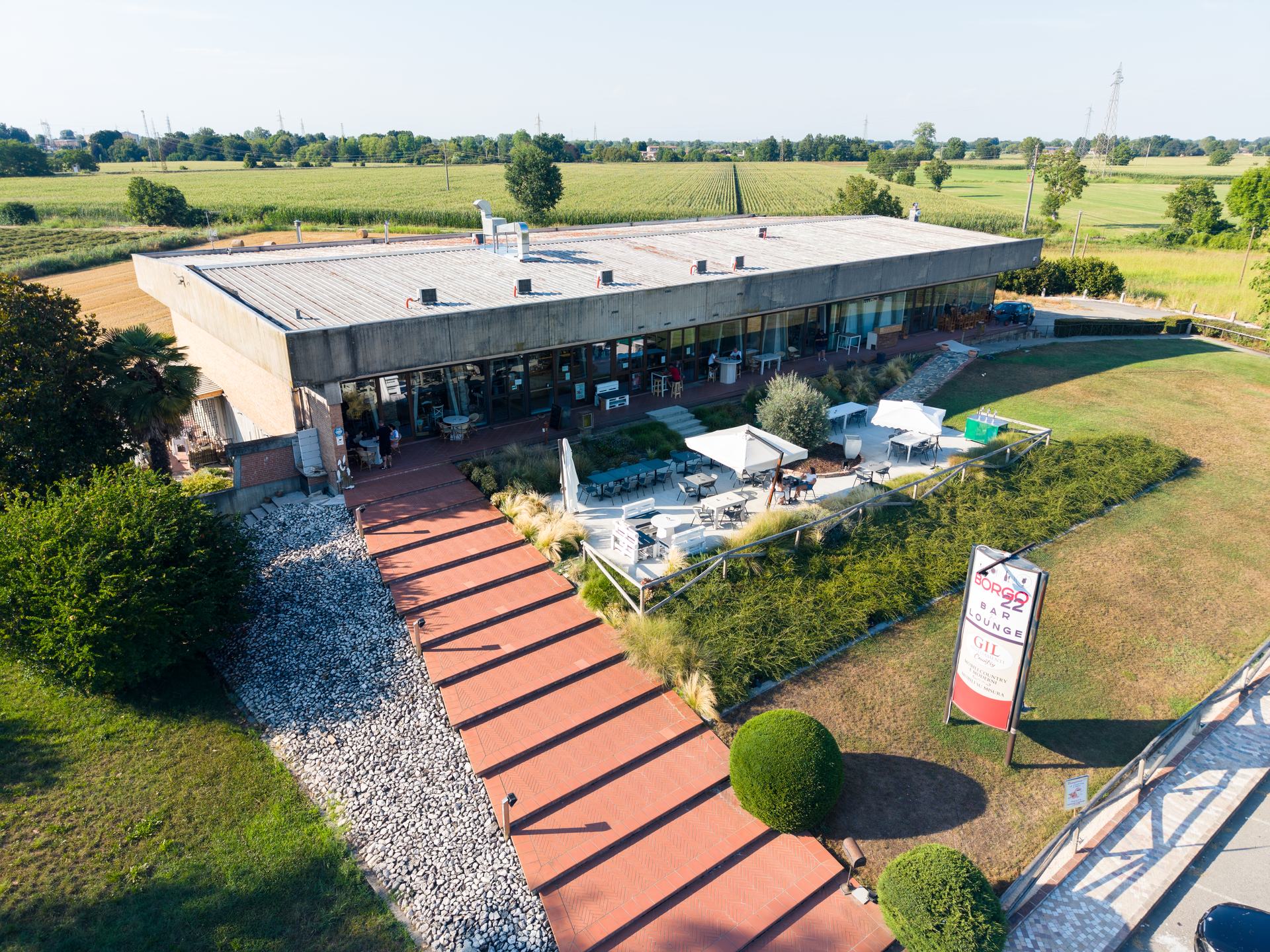 Borgo 22 Bar e Lounge al tramonto visto dal drone: il giardino con gli ombrelloni e il vialetto d'ingresso, a Monticelli d'Ongina